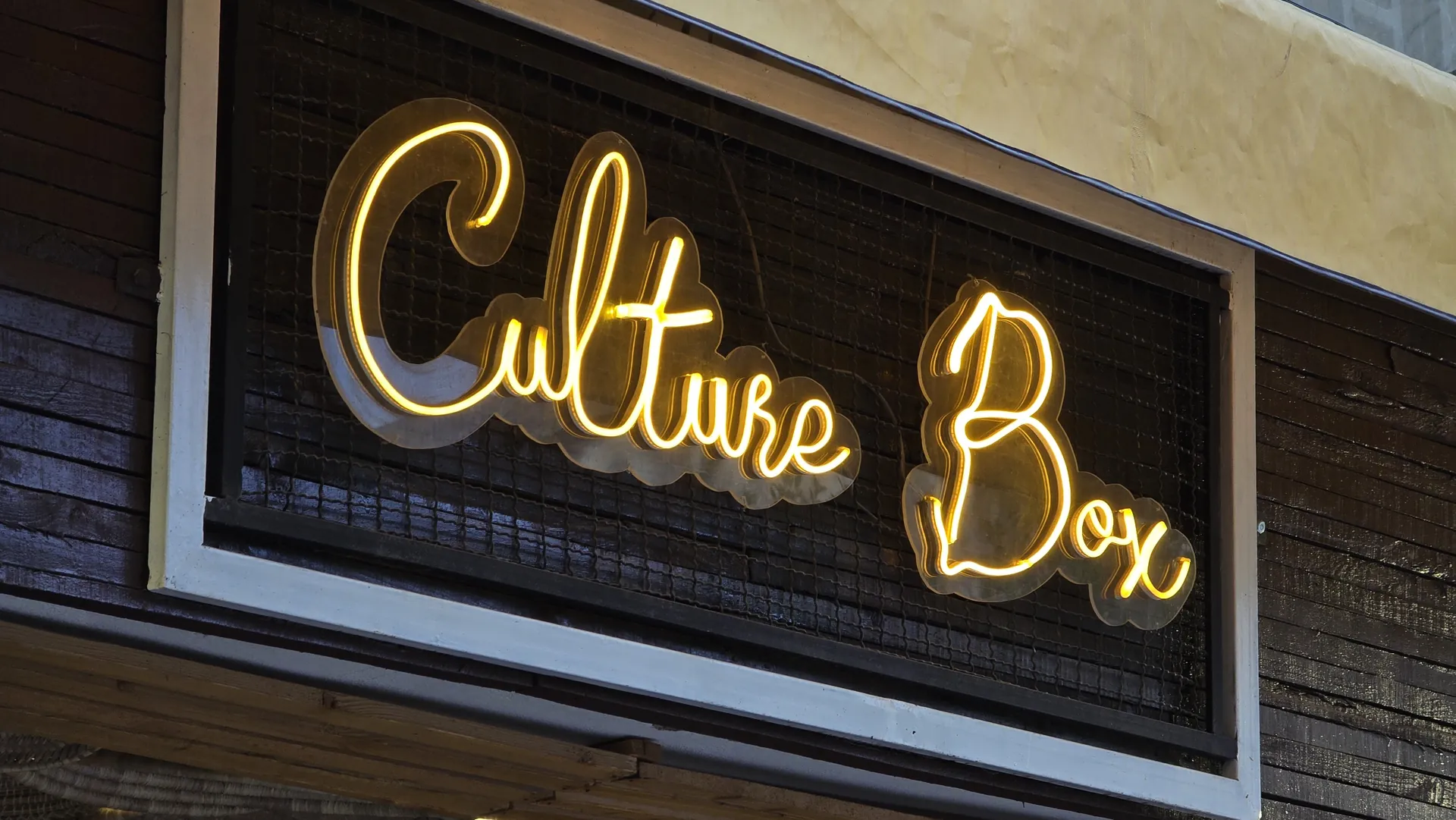 The yellow neon Culture Box sign glowing on its dark brick wall at night